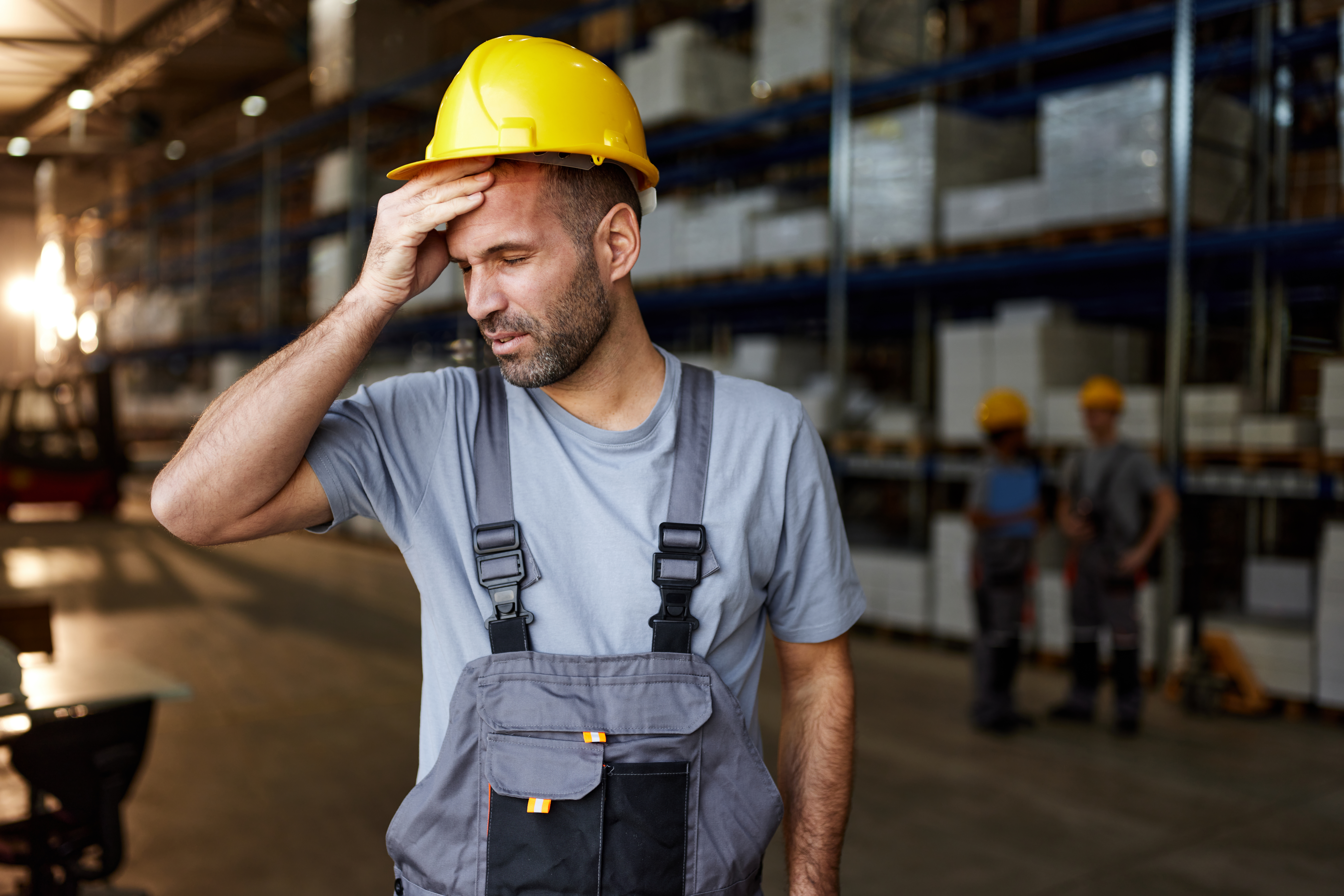 Exhausted manual worker holding his head in pain while working in distribution warehouse.